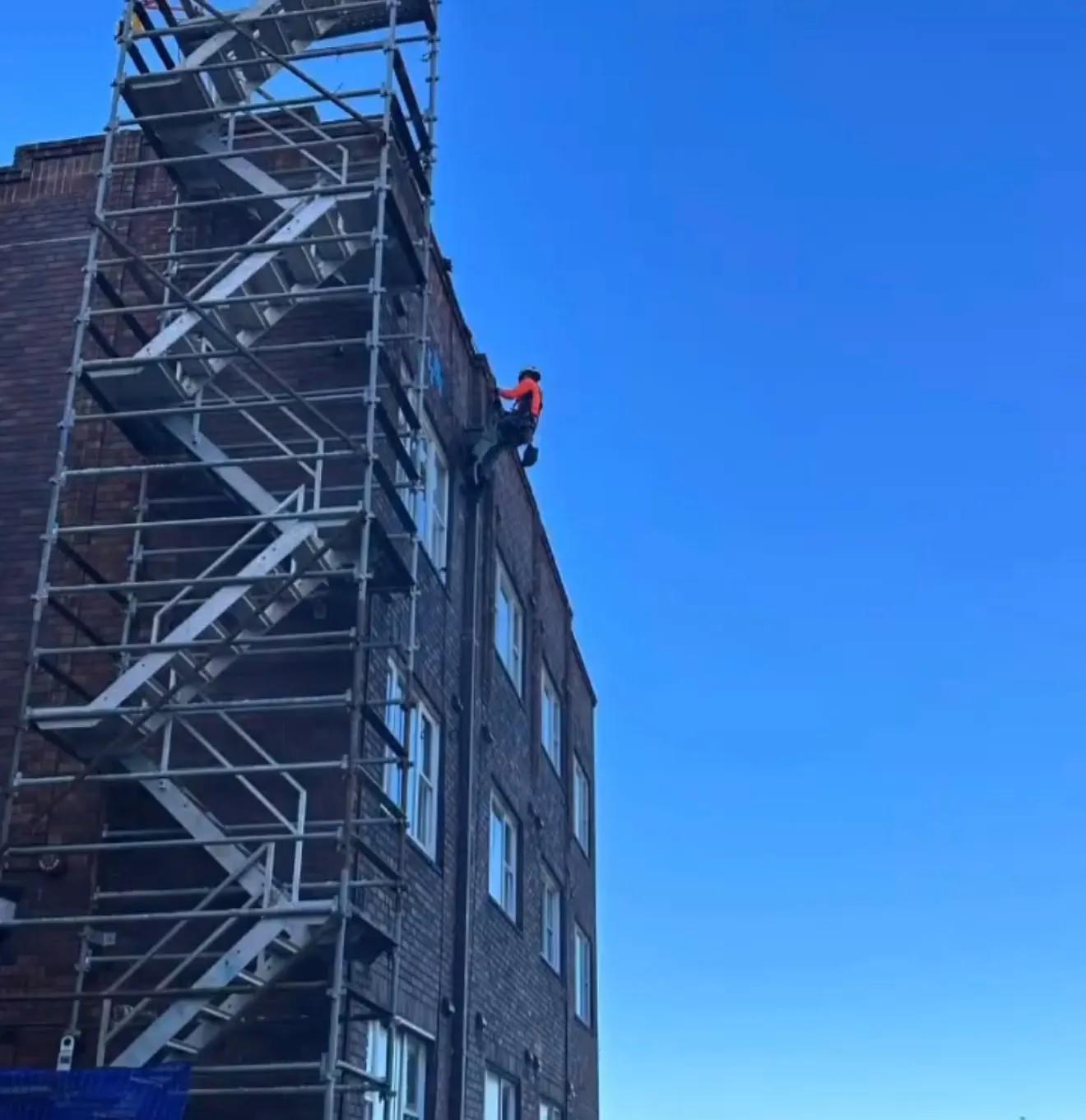 Technician on rope repointing the brickwork of an older apartment building