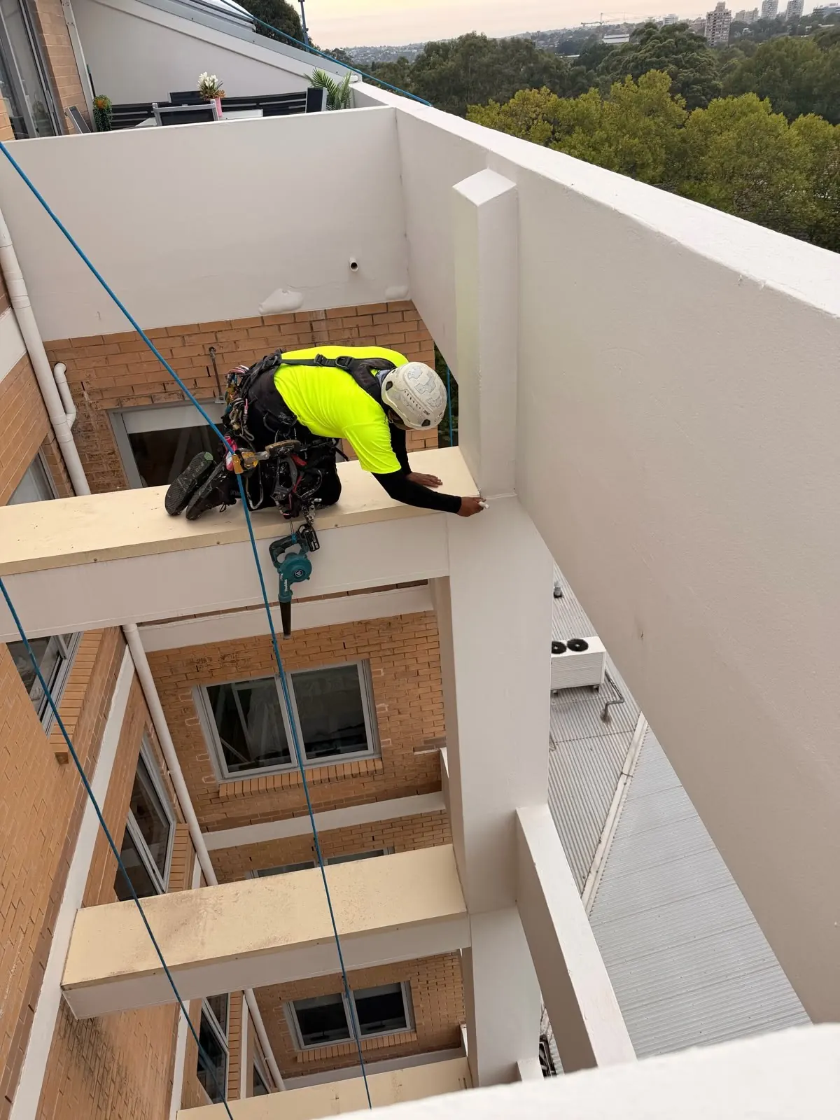 Waterproofing on rope: technician sealing a balcony beam joint