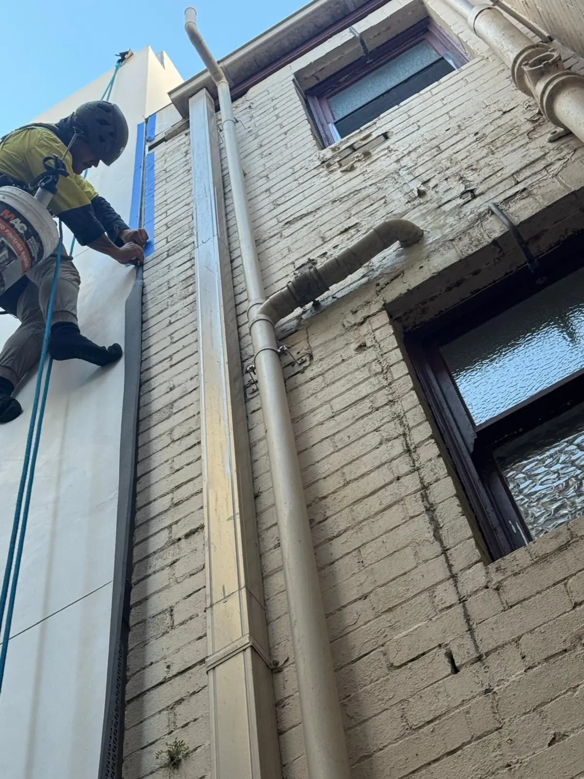 Leak sealing on rope: technician sealing joints on a brick building