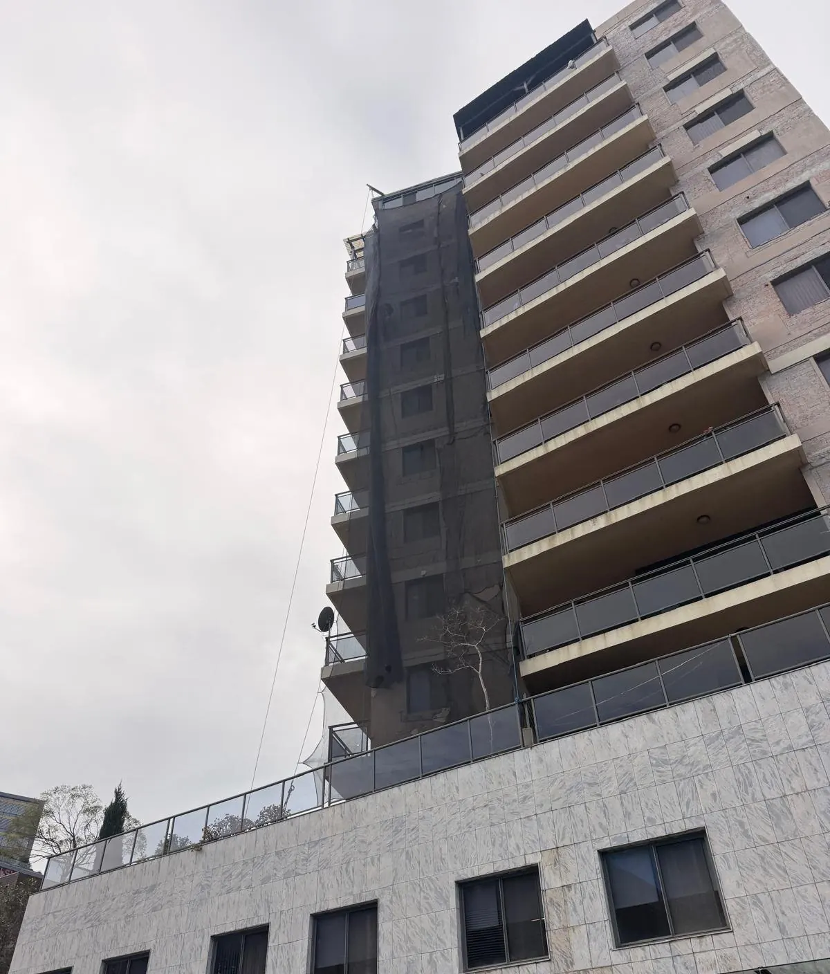 Residential tower with netting on one elevation during concrete repairs
