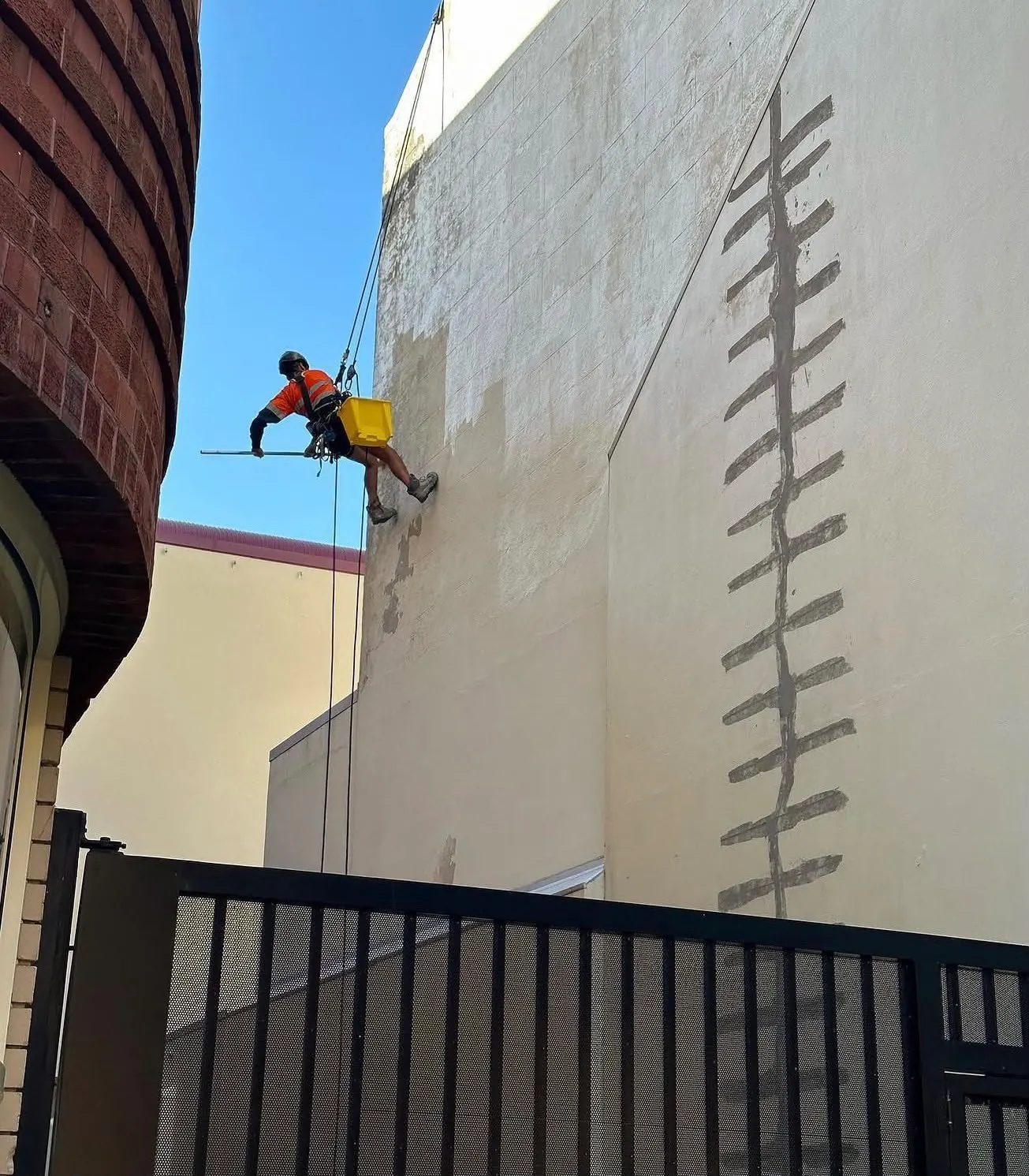 Technician on rope coating a rendered wall over stitched crack repairs
