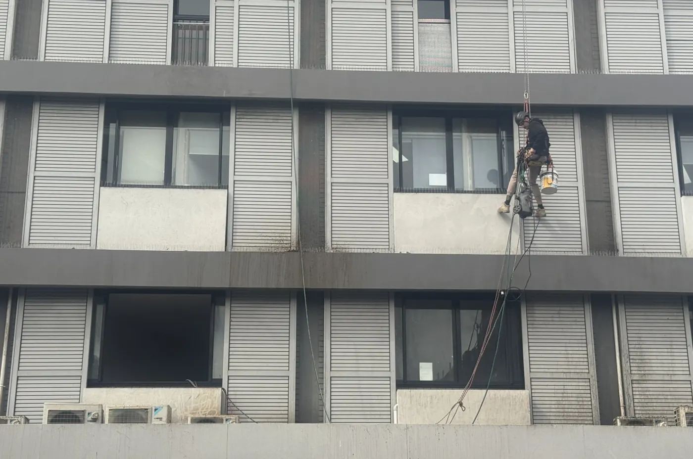 Technician on rope at a window ledge on the louvred façade of a Randwick hotel