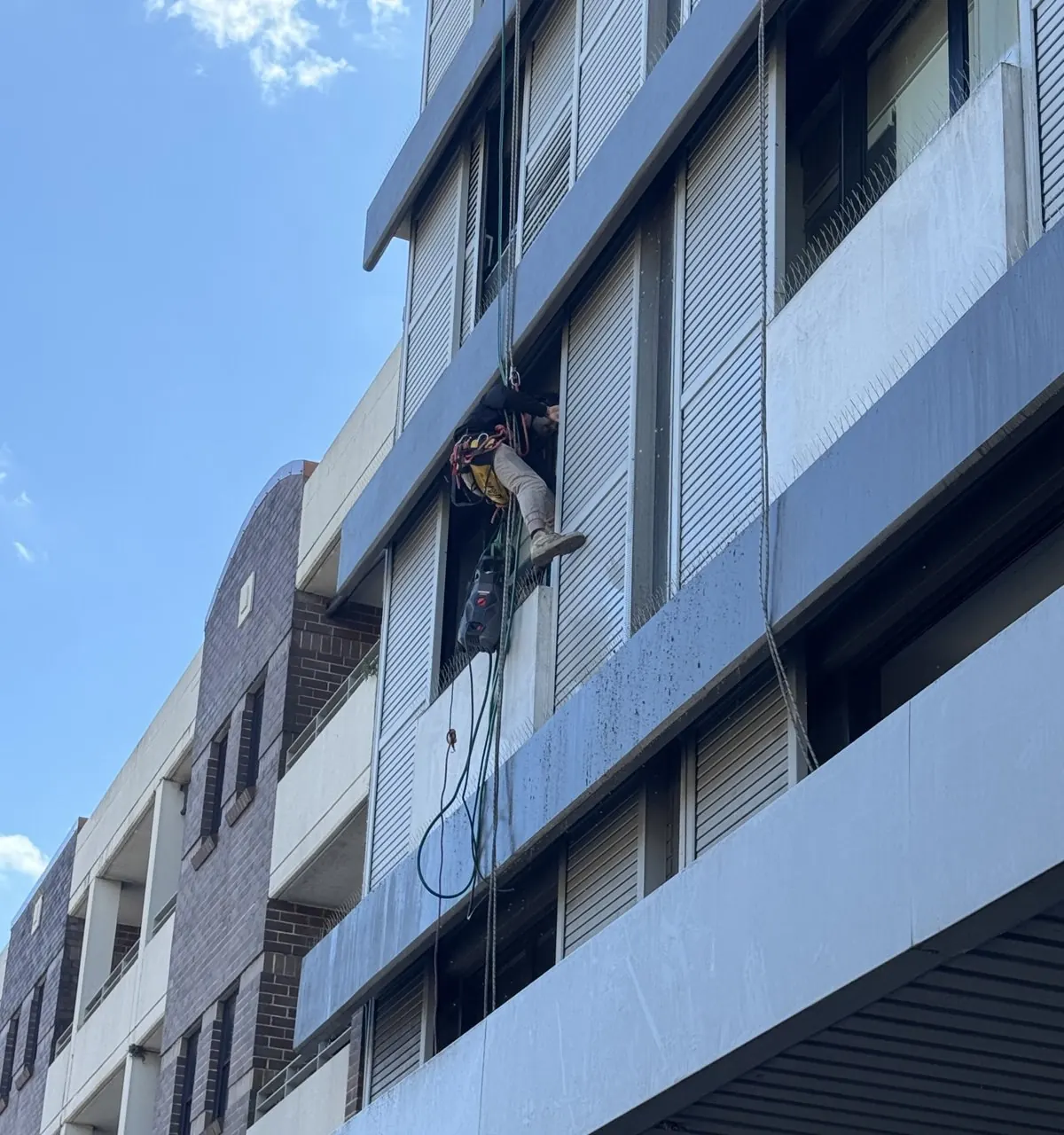 Rope access technician clearing the ledges of a hotel above the shops in Randwick
