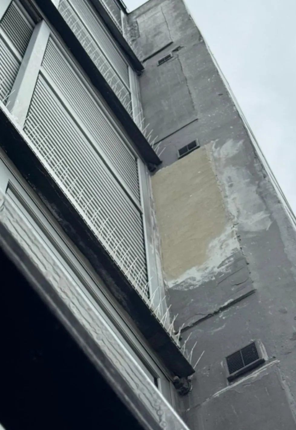 Render patch repair beside louvred windows, with bird spikes fitted along the ledges