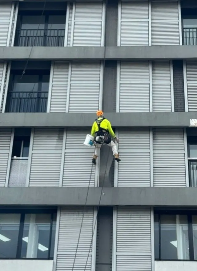 Technician on rope with a bucket working down the louvred hotel façade in Randwick