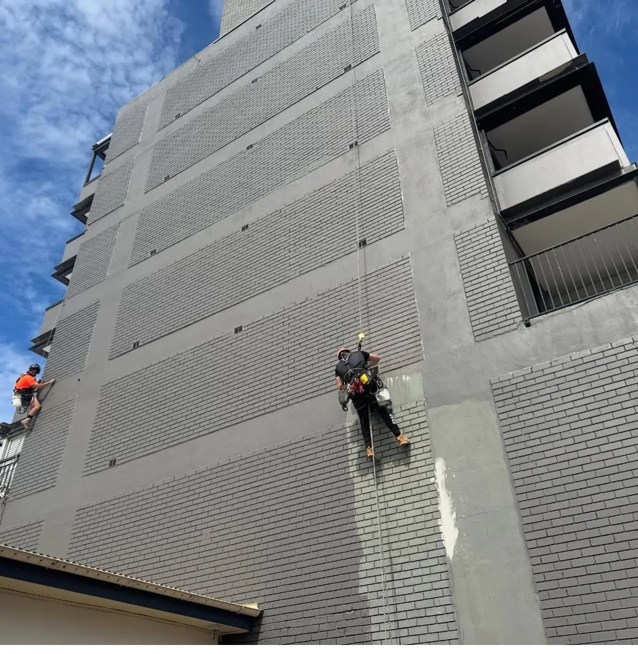 Rope access painter repainting the brick façade of a residential tower in Randwick