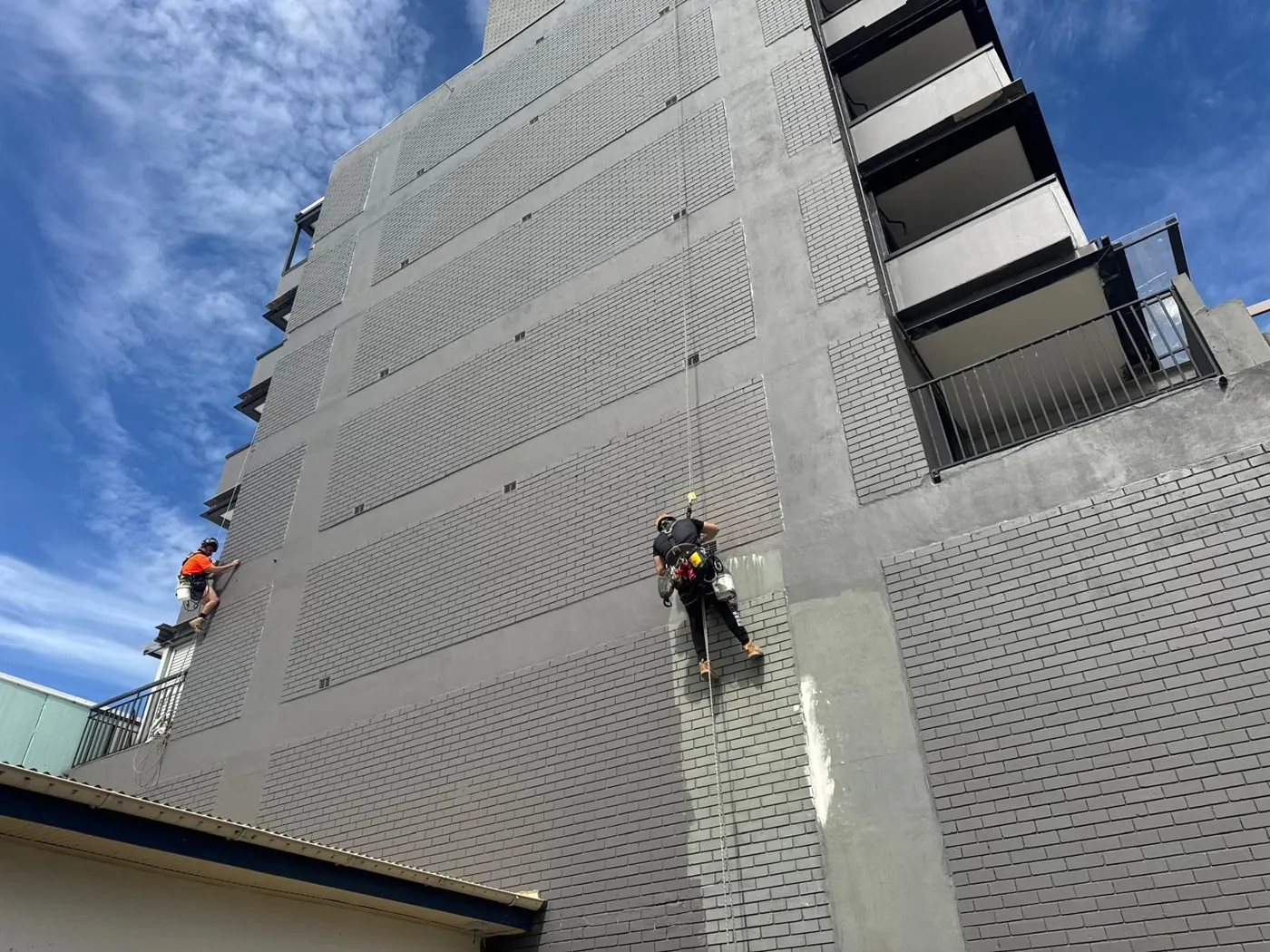 Two rope access painters repainting the brick façade of a tall residential tower in Randwick