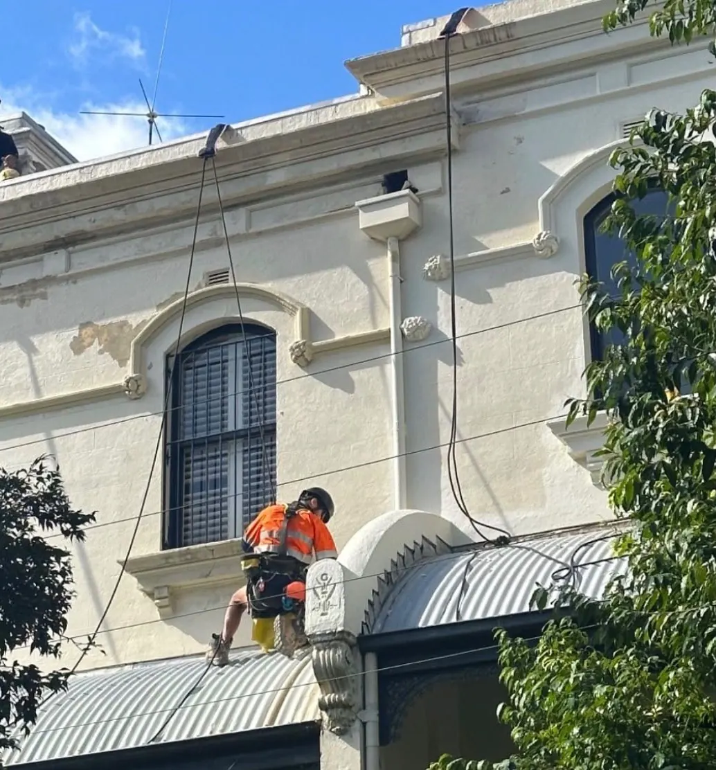 Painter on rope working on the heritage façade of a Redfern terrace, just above the street awning