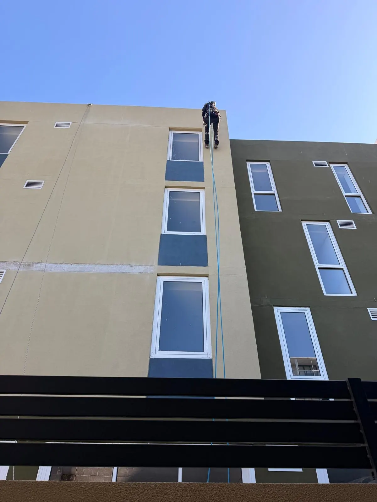 Technician on rope at the parapet of a 4-storey residential building during render and joint repairs
