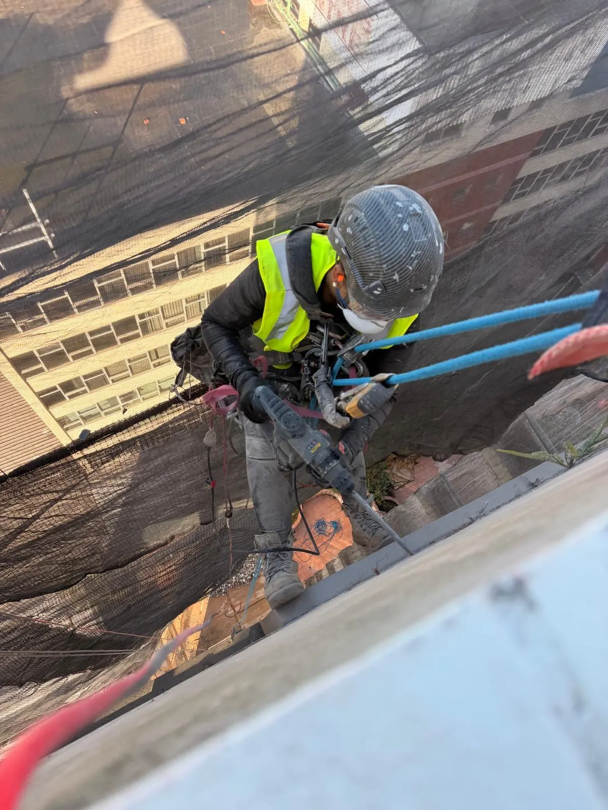 Technician on rope breaking out and repairing concrete cancer on a high-rise façade