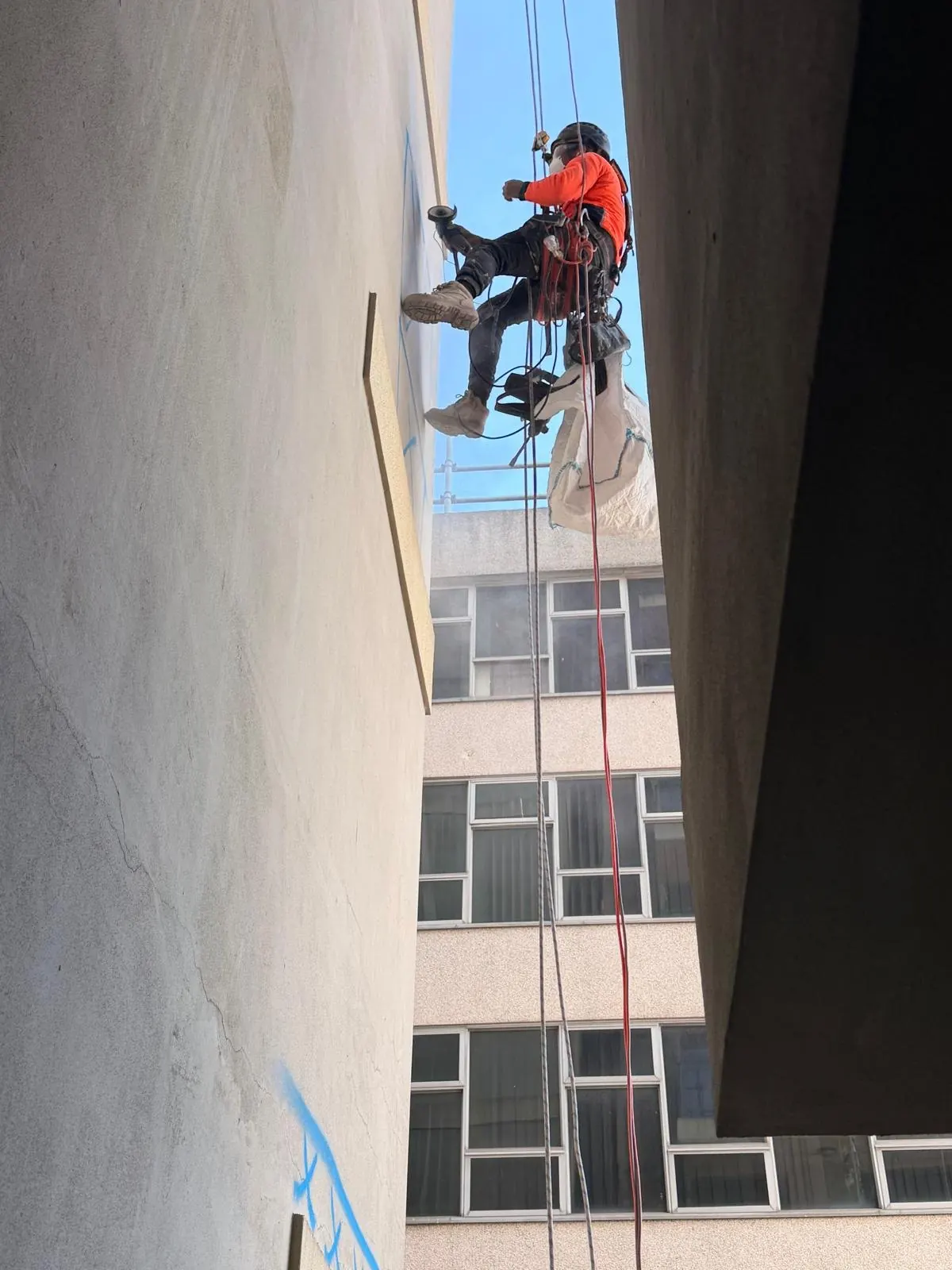 Façade inspection on rope: technician checking a rendered wall, with defects marked in blue below