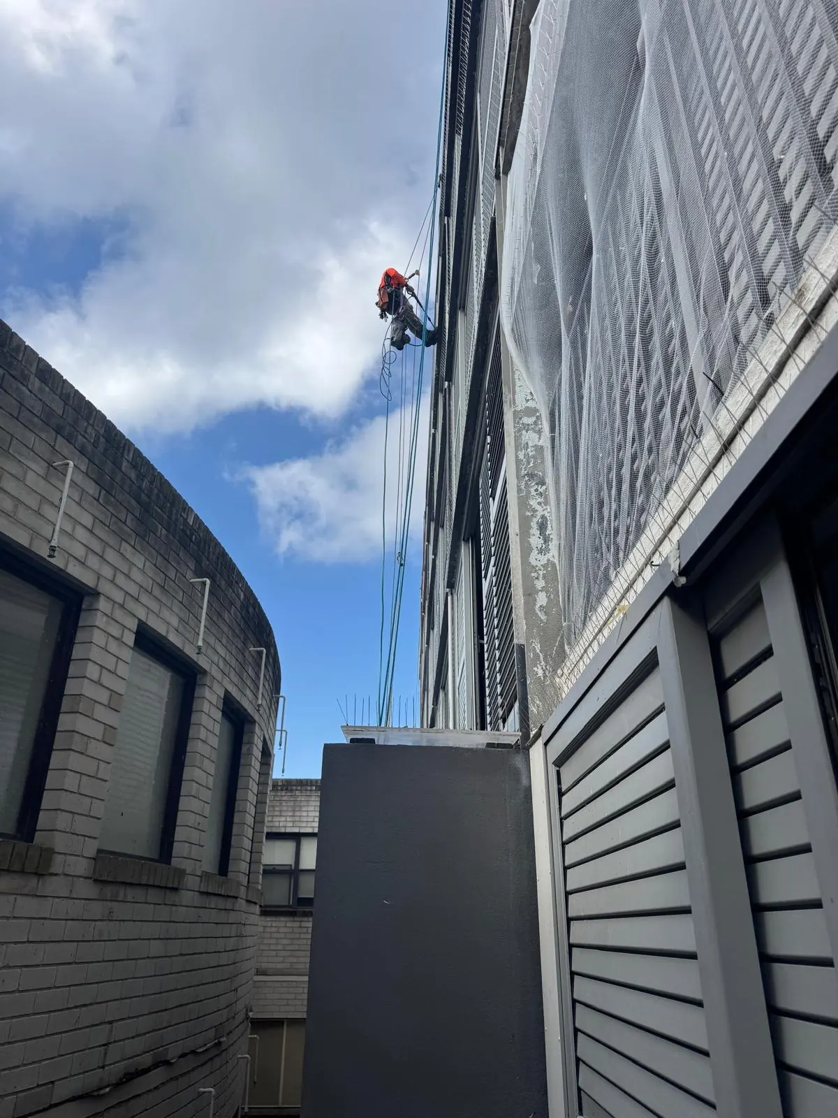 Rope access technician working high on a screened commercial façade