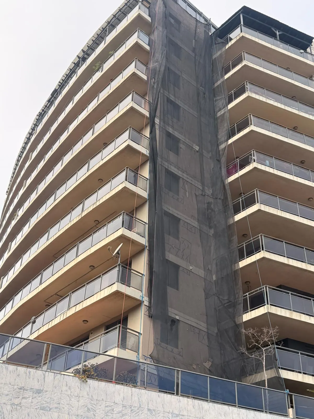 Containment netting down a curved residential tower during remedial works