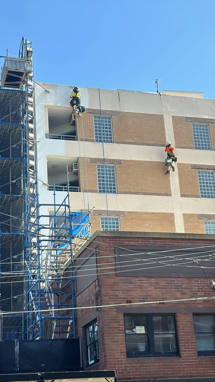 Two rope access technicians working on a façade beside scaffolding on a construction site